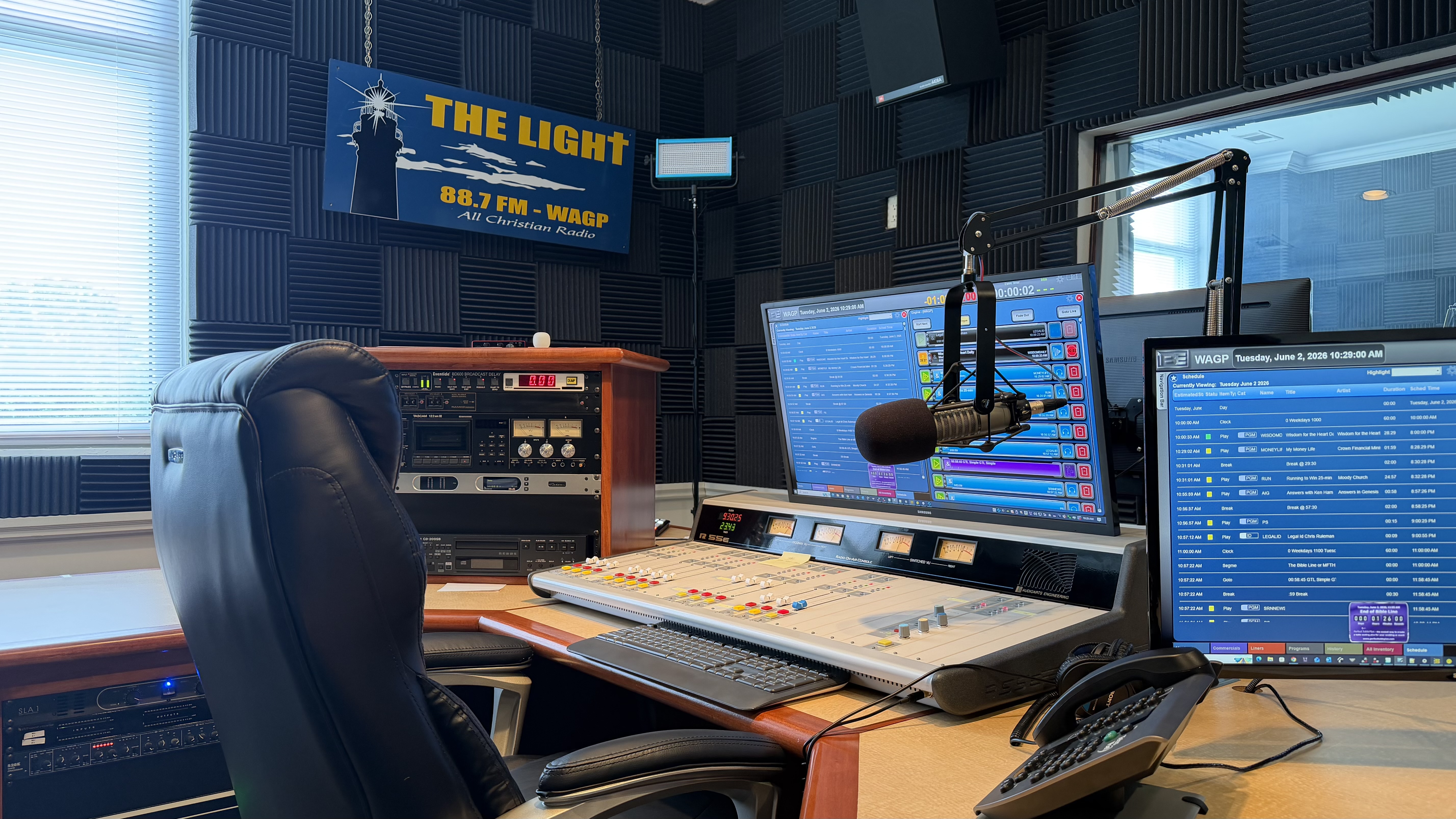Close view of broadcast microphone, mixing console, and station monitors